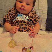 Dream is registered to the contest to win money with this photo: baby, infant, leopard_print, nike_shirt, gold_necklace, pacifier, blanket, bed, curly_hair, cute, lying_down, soft_lighting, indoors, child, human, portrait, clothing, accessory, skin, face