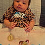 baby, infant, leopard_print, nike_shirt, gold_necklace, pacifier, blanket, bed, curly_hair, cute, lying_down, soft_lighting, indoors, child, human, portrait, clothing, accessory, skin, face