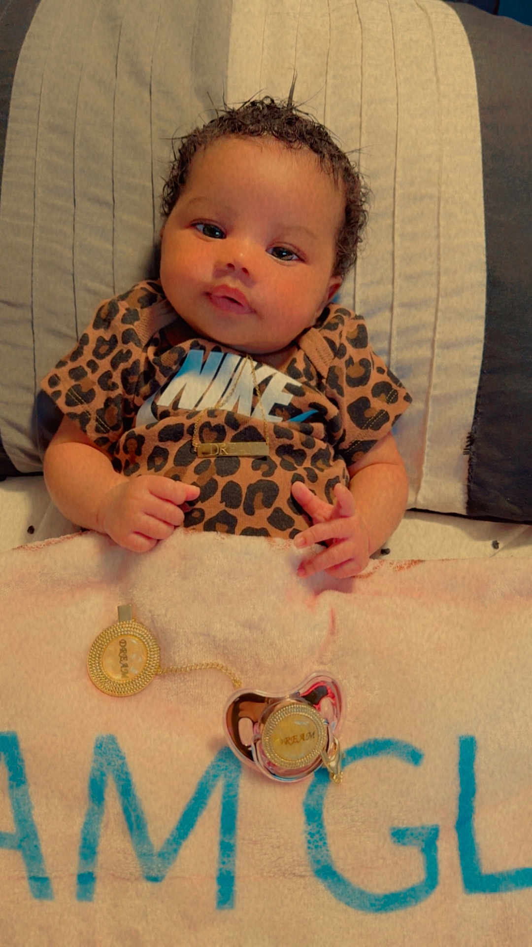 Dream is registered to the contest to win money with this photo: baby, infant, leopard_print, nike_shirt, gold_necklace, pacifier, blanket, bed, curly_hair, cute, lying_down, soft_lighting, indoors, child, human, portrait, clothing, accessory, skin, face