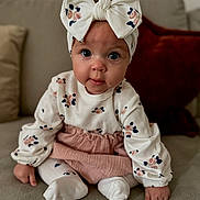 Elouise is registered to the contest to win money with this photo: baby, bow, child, clothing, couch, cute, face, floral_pattern, hands, headband, indoors, infant, person, pink, portrait, sitting, sofa, tights, white, young_child