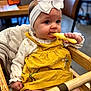Elouise joined the competition — help win amazing prizes! baby, bow, child, clothing, curious, cute, expression, face, hand, headband, high_chair, indoor, infant, munching, person, portrait, seated, snack, wooden_furniture, yellow_dress