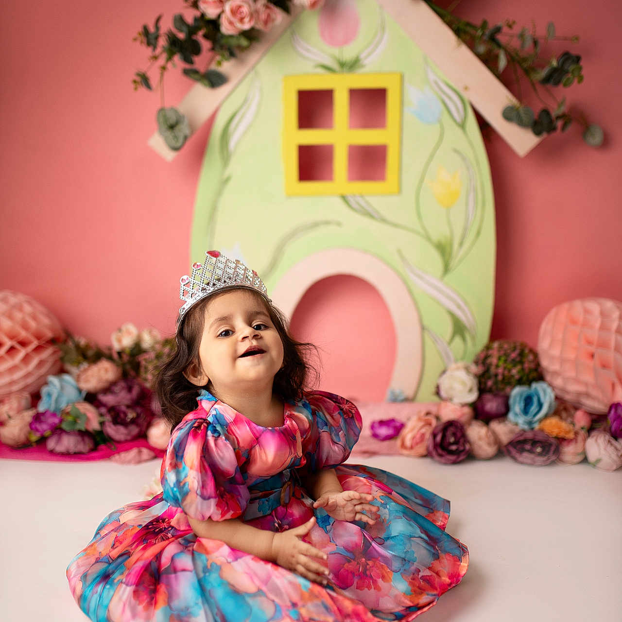 Tiana is registered to the contest to win money with this photo: celebration, child, colorful, cute, decor, dress, floral_dress, flower, girl, happy, indoor, innocence, pink_background, playful, portrait, sitting, smiling, tiara, toddler, young_child