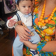 Mattia a rejoint le concours — aidez-le/la à gagner de superbes lots ! baby, child, person, adult, hand, clothing, hat, dress, necklace, indoor, banner, floor, wooden_floor, toy, socks, blue, orange, pattern, holding, curious