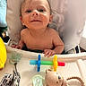 Brian is registered to the contest to win money with this photo: baby, high_chair, smile, toy, pacifier, infant, child, cute, happy, face, hand, blue_eyes, skin, indoor, furniture, feeding_chair, playtime, adorable, closeup, person