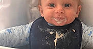 Brian joined the competition — help win amazing prizes! baby, child, high_chair, bib, food, messy, blue_eyes, face, feeding, infant, cute, smiling, clothing, indoor, person, young_child, smudge, table, seat, meal