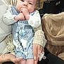 Logan is registered to the contest to win money with this photo: baby, child, person, infant, holding, clothing, blue_booties, pacifier, name_tag, restaurant, table, food, fries, young_child, hands, seated, casual, indoor, family, cute
