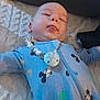 baby, child, infant, blue_onesie, mickey_mouse, pacifier_clip, blanket, knitted, couch, tongue_out, smiling, person, indoor, cute, sleepy, relaxed, face, head, baby_clothing, lying_down
