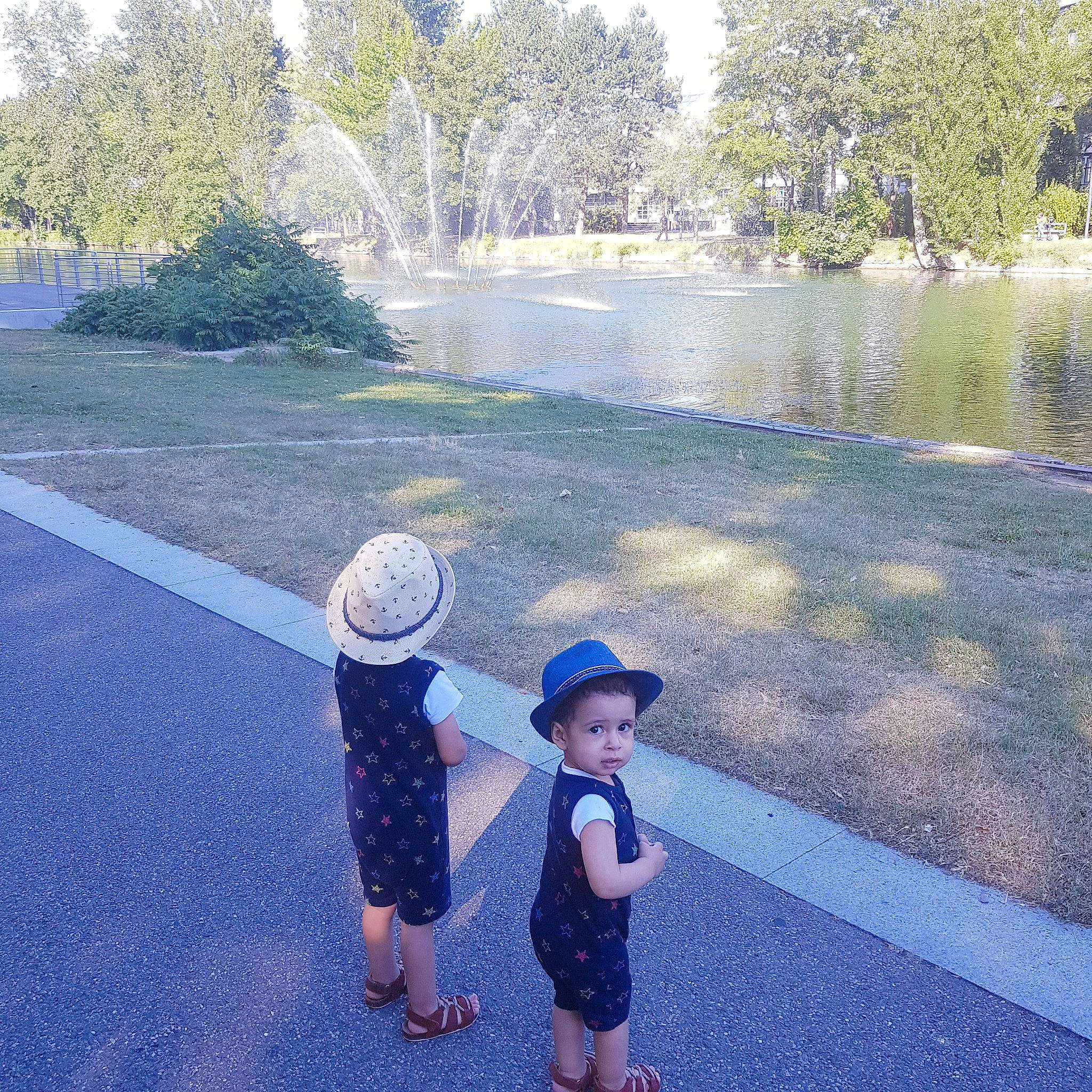 Anis participe au concours pour gagner de l'argent avec cette photo : asphalt, body_of_water, botany, grass, hat, leaf, leisure, natural_environment, nature, people_in_nature, person, plant, public_space, road_surface, sky, sun_hat, sunlight, toddler, tree, water