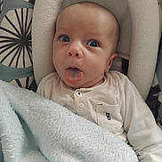 Eden participe au concours pour gagner de l'argent avec cette photo : baby, infant, tongue_out, blanket, white_clothing, seat, patterned_background, cute, child, face, blue_eyes, soft_texture, cozy, portrait, expression, indoors, newborn, small_hands, buttoned_shirt, comfort