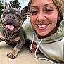 woman, dog, french_bulldog, smiling, happy, outdoor, selfie, tongue_out, curly_hair, piercings, hoodie, chain_collar, concrete, trees, cloudy_sky, face, closeup, pet, friendship, casual
