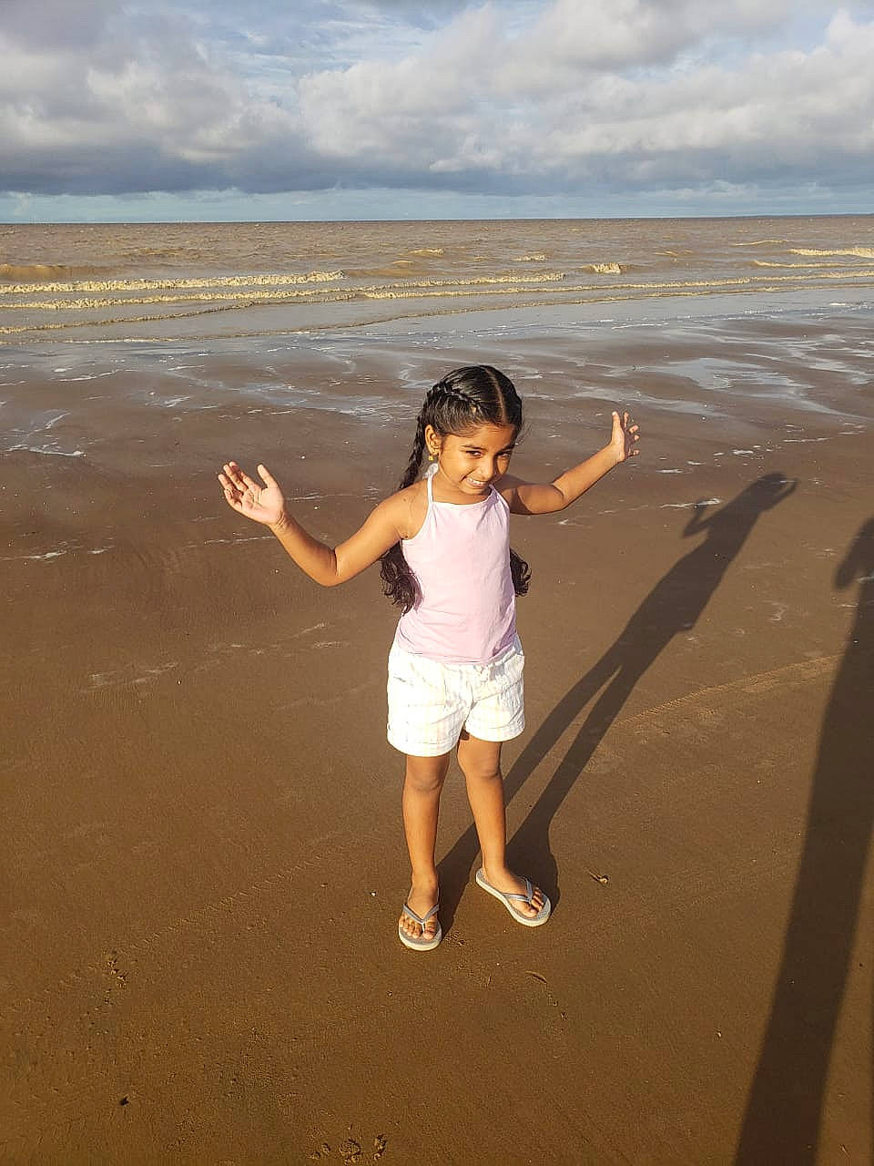 Shaniya is registered to the contest to win money with this photo: azure, beach, cloud, flash_photography, fun, gesture, happy, horizon, joy, leisure, people_in_nature, people_on_beach, person, shore, shorts, sky, smile, standing, toddler, travel