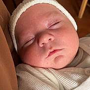 Francky a rejoint le concours — aidez-le/la à gagner de superbes lots ! baby, sleeping, infant, white_hat, white_sweater, close_up, face, peaceful, soft_lighting, cozy, knitwear, newborn, child, portrait, indoor, resting, cute, warm_colors, skin, calm