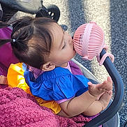Amelia joined the competition — help win amazing prizes! biting, blanket, casual, child, colorful_clothing, curious, daylight, feet, ground, outdoor, person, pigtails, pink_fan, playful, seat, shadow, shoes, stroller, toddler, toy