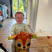 Jöy participe au concours pour gagner de l'argent avec cette photo : child, cute, daylight, door, floor, furniture, happy, home, indoor, kitchen, lion_king, pajamas, person, play, ride_on_toy, smiling, tile_floor, toddler, toy, window