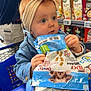 baby, child, shopping_cart, headband, bow, grocery_store, snack_bag, dog_treats, blue_jacket, shelf, bottles, carton, curious, shopping, retail, person, indoor, food_package, young_child, cute