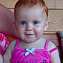 child, toddler, blue_eyes, red_hair, pink_tank_top, white_bow, flower_text, smile, wooden_background, indoor, person, cute, baby, portrait, happy, face, skin, sleeveless, sitting, casual
