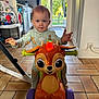 toddler, child, toy, indoor, floor, pajamas, deer_toy, wheels, kitchen, doorway, garden, window, tile_floor, play, cute, happy, person, furniture, light, expression