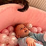 baby, child, ball_pit, pink_balls, white_balls, cat_tail, soft_fabric, indoor, playtime, cute, happy, smiling, blue_eyes, infant, toy, relaxing, cozy, pastel_colors, curious_cat, comfort