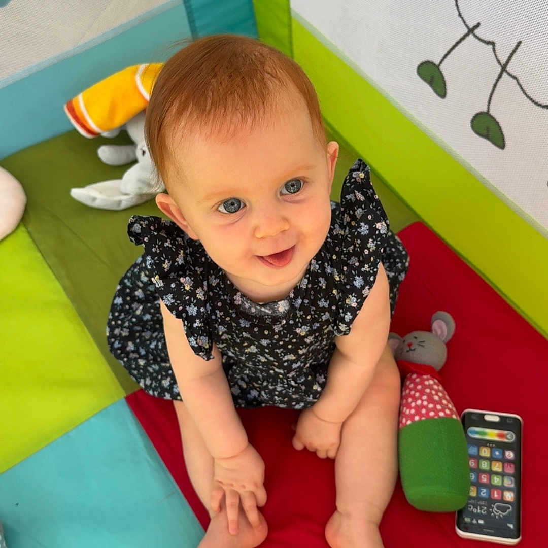 Jöy a rejoint le concours — aidez-le/la à gagner de superbes lots ! baby, blue_eyes, child, colorful_mat, cute, dress, illustration, indoor, infant, looking_up, numbers, patterned_clothing, playful, playpen, plush_toy, short_hair, sitting, smiling, soft_toys, toy_phone