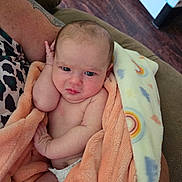 Athena is registered to the contest to win money with this photo: baby, infant, blanket, peach_blanket, rainbow_pattern, tattoo, arm, couch, wooden_floor, diaper, skin, person, indoors, holding, cute, expression, face, hand, comfort, resting