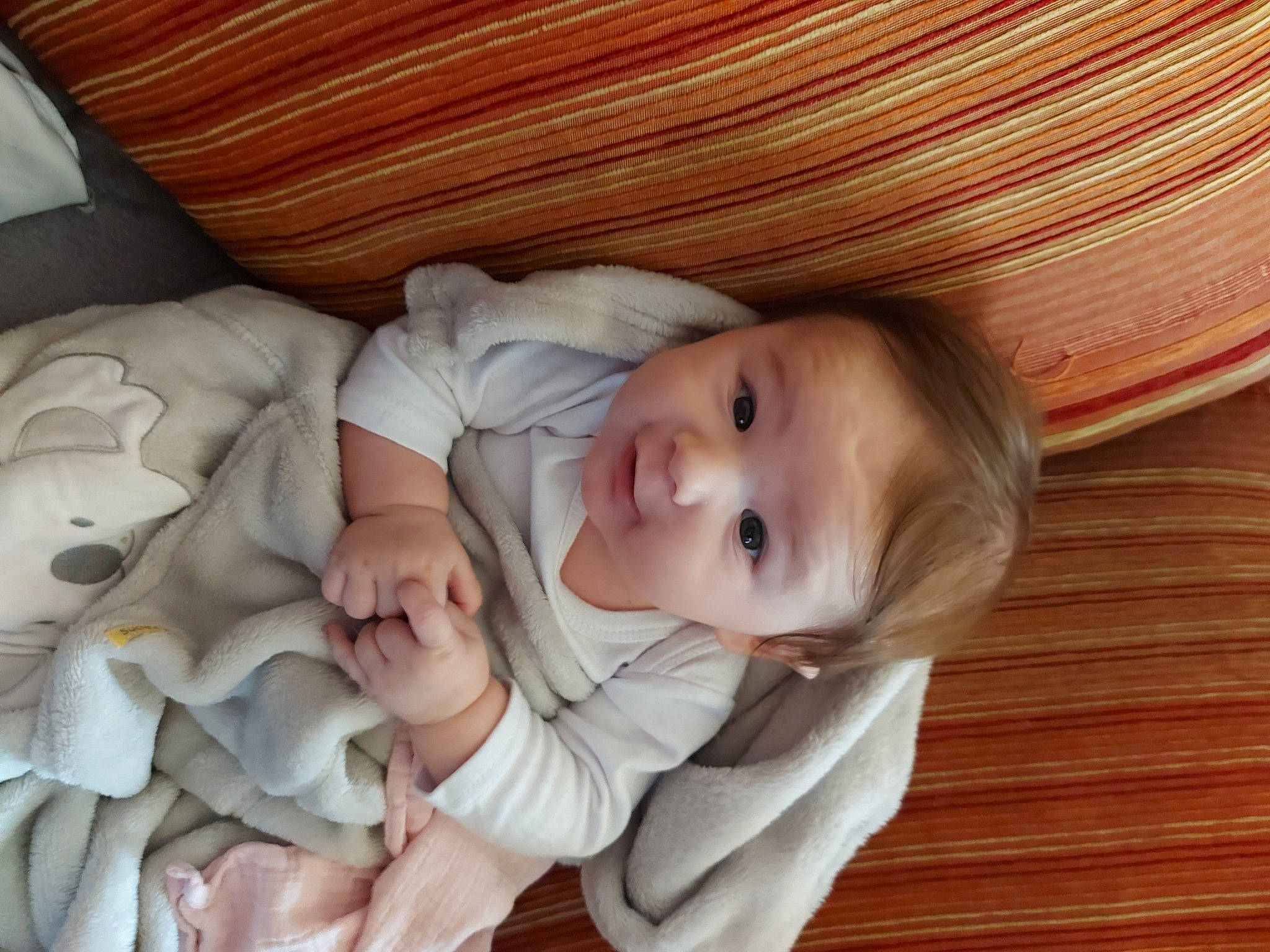 Eyden participe au concours pour gagner de l'argent avec cette photo : baby, baby_toddler_clothing, cheek, child, comfort, eye, flooring, gesture, happy, hardwood, head, linens, person, sitting, sleeve, smile, textile, thumb, toddler, varnish