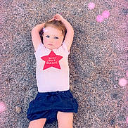 Aurora is registered to the contest to win money with this photo: child, lying_down, gravel, white_shirt, red_star, shorts, outdoor, pink_overlay, glowing_orbs, arms_up, casual_clothing, young_child, magic, face, legs, summer, cute, portrait, expression, relaxed