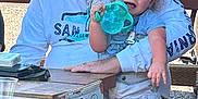 Tannen joined the competition — help win amazing prizes! toddler, child, man, adult, outdoor, picnic_table, sippy_cup, sign, casual_clothing, hat, tattoos, seating, daylight, bench, smiling, family, holding, sunlight, relaxed, beard