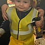 Tannen is registered to the contest to win money with this photo: toddler, child, yellow_hat, yellow_vest, toy_hammer, indoor, person, hand_support, red_pants, white_shoes, wooden_floor, costume, smile, face, curly_hair, play, casual, home, fun, blurry