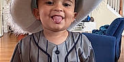 Yamari is registered to the contest to win money with this photo: toddler, child, hat, costume, indoor, tongue_out, smiling, spiderman, jersey, person, furniture, living_room, blue_chair, wooden_floor, playful, cute, apparel, young_child, portrait, home