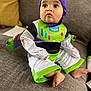 baby, child, costume, buzz_lightyear, purple_hood, green, white, couch, indoor, foot, sitting, curious, face, cute, clothing, pants, long_sleeve, toy_story, person, infant