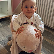 Myla participe au concours pour gagner de l'argent avec cette photo : baby, child, plush_toy, rocking_toy, bunny, wooden_floor, indoor, furniture, radiator, white_sweater, smiling, cute, hands, flooring, room, toy, baby_clothes, home, childhood, infant