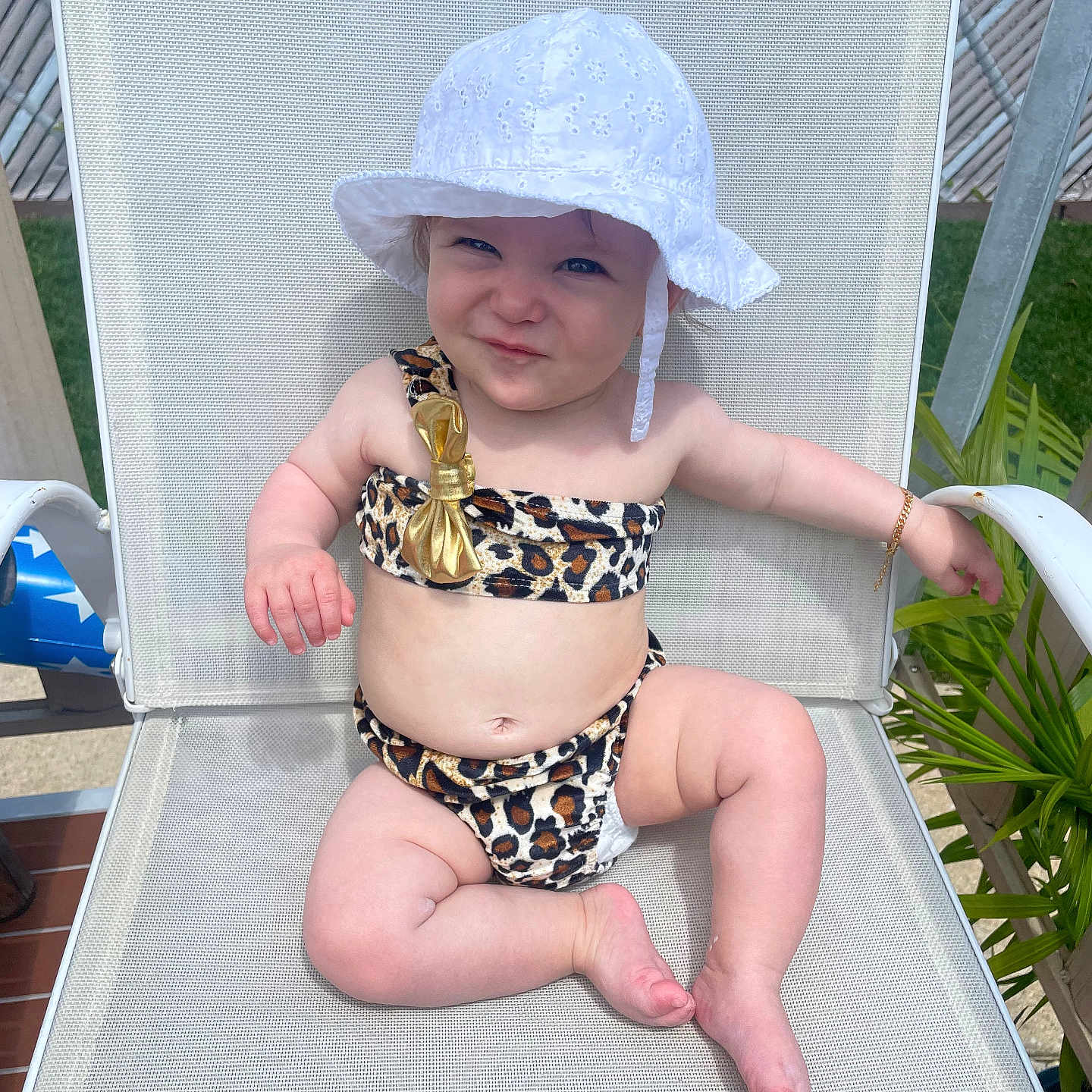 Vianna is registered to the contest to win money with this photo: baby, bikini, bracelet, chair, child, face, fashion, foot, green_plant, hand, leopard_print, mesh_chair, outdoor, person, relaxing, skin, smile, summer, sunlight, white_hat