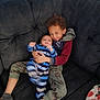Maverick is registered to the contest to win money with this photo: child, baby, couch, hug, smile, happy, indoor, clothing, striped_pajamas, socks, curly_hair, sibling, family, cozy, blanket, casual_wear, playful, home, comfort, portrait