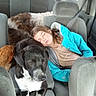Blackjack is registered to the contest to win money with this photo: child, dog, sleeping, car_interior, seat, seatbelt, jacket, window, pet, animal, resting, cozy, travel, road_trip, fur, black_and_white, brown_dog, curled_up, relaxed, companion