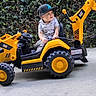 Marcelino is registered to the contest to win money with this photo: child, toddler, boy, outdoor, toy, excavator, construction_vehicle, ride_on_toy, yellow, black, cap, shirt, smiling, sitting, driveway, hedge, garden, wheels, playtime, portrait