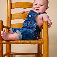 Riley is registered to the contest to win money with this photo: baby, child, smile, denim_overalls, rocking_chair, wooden_chair, happy, cute, infant, portrait, sitting, foot, hand, blue_eyes, studio, indoors, clothing, person, furniture, toddler