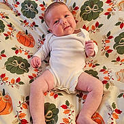 Isabella joined the competition — help win amazing prizes! baby, infant, onesie, smile, face, legs, arms, blanket, pumpkin, leaf_pattern, autumn, cute, child, person, skin, lying_down, indoors, happy, chubby, comfortable
