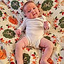 baby, infant, onesie, smile, face, legs, arms, blanket, pumpkin, leaf_pattern, autumn, cute, child, person, skin, lying_down, indoors, happy, chubby, comfortable