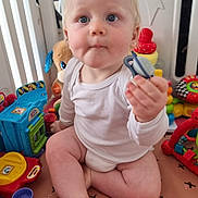 Lucas a rejoint le concours — aidez-le/la à gagner de superbes lots ! baby, child, pacifier, toys, playpen, plush_toy, play_mat, indoor, curious, sitting, white_clothing, blond_hair, blue_eyes, infant, colorful, plastic_toys, floor, cute, young_child, expression