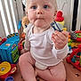 baby, child, pacifier, toys, playpen, plush_toy, play_mat, indoor, curious, sitting, white_clothing, blond_hair, blue_eyes, infant, colorful, plastic_toys, floor, cute, young_child, expression