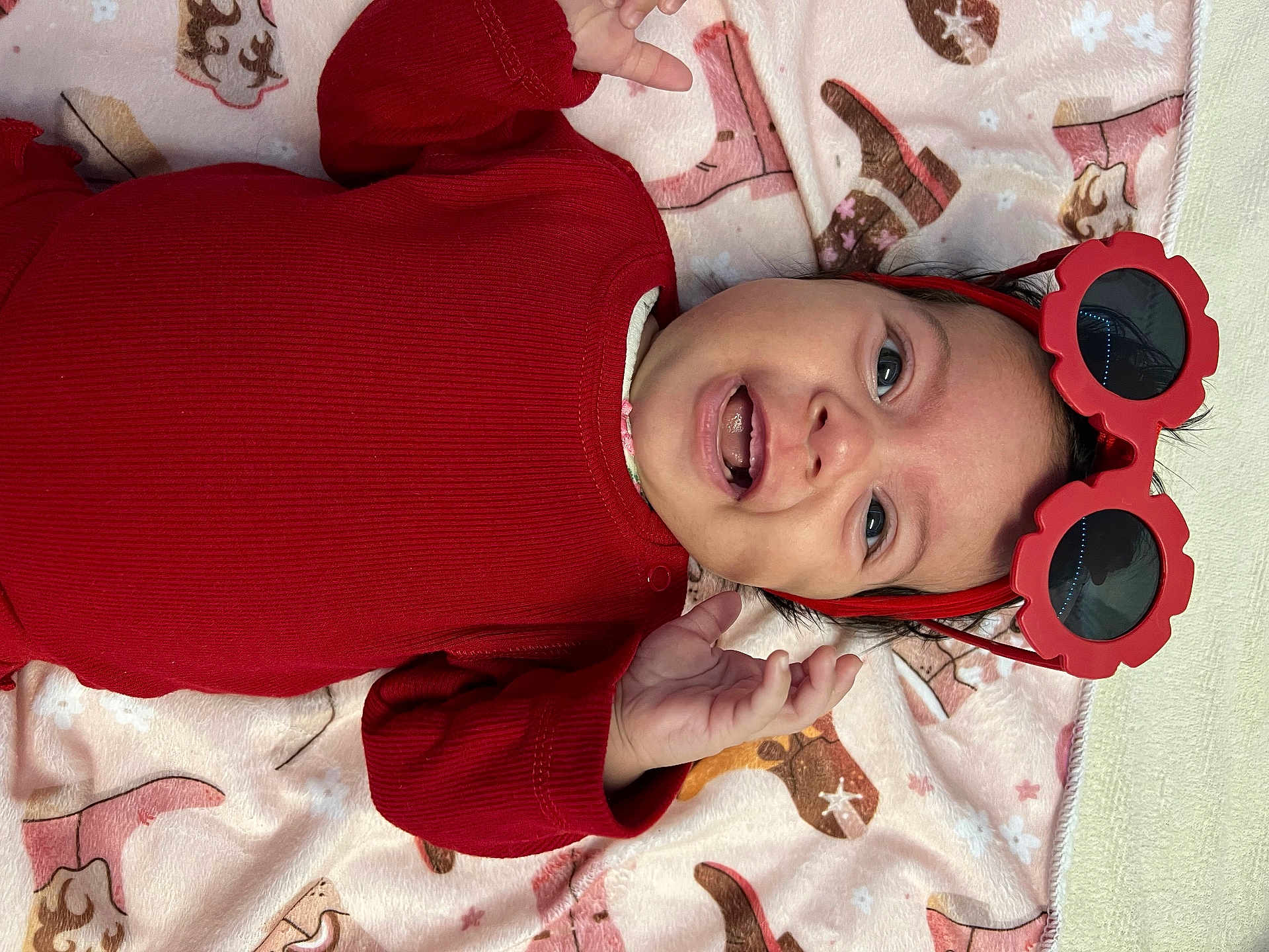 Eva Cecília joined the competition — help win amazing prizes! baby, blanket, child, cowboy_boots, cute, face, hand, happy, headband, indoor, infant, lying_down, pattern, person, portrait, red_clothing, smile, star_pattern, sunglasses, teeth