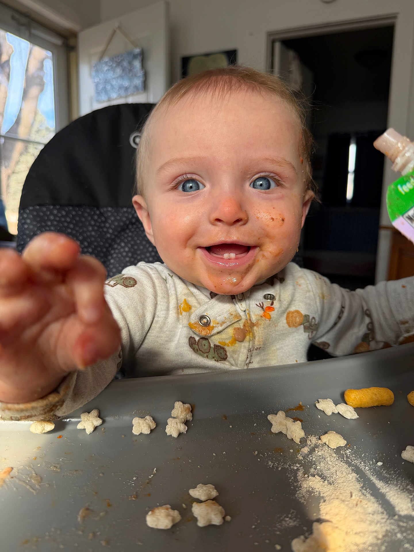 Jensen is registered to the contest to win money with this photo: baby, toddler, child, highchair, messy, food_smear, blue_eyes, smile, teeth, reaching_hand, tray, snack, cereal, puree_pouch, bib, indoor, window, portrait, closeup, happy