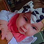 baby, child, headband, bow, pink_clothing, white_clothing, face, hands, indoor, wooden_surface, curious, cute, young_child, portrait, person, infant, chubby_cheeks, table, closeup, home