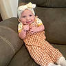 baby, child, headband, bow, smile, couch, furniture, clothing, socks, portrait, infant, happy, indoors, cute, person, seated, cozy, orange_checkered, headwear, relaxing