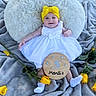 baby, infant, child, white_dress, yellow_headband, smiling, pillow, blanket, outdoor, grass, yellow_roses, flowers, wooden_sign, celebration, milestone, happy, cute, socks, person, portrait