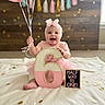 Imogen joined the competition — help win amazing prizes! baby, girl, pink, balloons, headband, number_six, sign, confetti, blanket, tassel_garland, smiling, celebration, indoor, wooden_wall, decor, child, sitting, happy, festive, cute