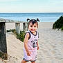 barefoot, beach, child, daylight, happy, nature, ocean, outdoor, pigtails, pink_outfit, playful, portrait, sand, sky, smile, sporty_clothing, summer, toddler, wooden_fence, young_child