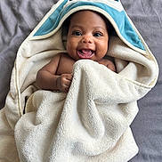 Noah is registered to the contest to win money with this photo: baby, infant, child, smiling, happy, portrait, face, eyes, hooded_blanket, blanket, towel, textile, cozy, lying_down, indoor, bed, gray_background, close_up, adorable, photography
