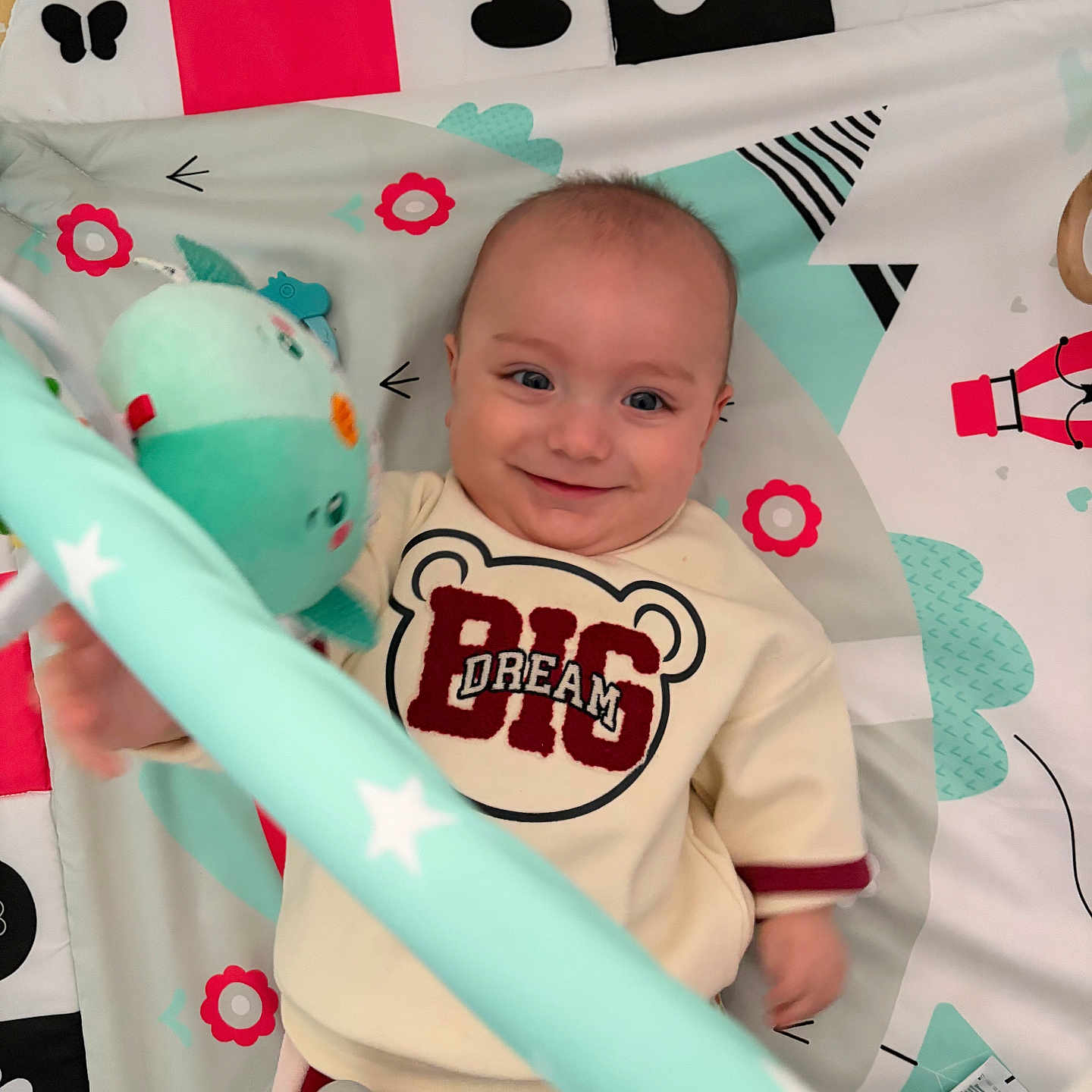 Zahit a rejoint le concours — aidez-le/la à gagner de superbes lots ! accessory, baby, clothing, cute, eyes, face, hand, happy, indoor, infant, lying_down, nursery, onesie, pattern, play_mat, plush, portrait, smiling, star_pattern, toy