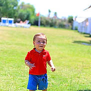 Miras a rejoint le concours — aidez-le/la à gagner de superbes lots ! child, toddler, smiling, red_shirt, blue_shorts, mickey_mouse, grass, lawn, sunny, outdoors, park, daylight, play, baby_hands, face, portrait, vacation, resort, sunlounger, bright
